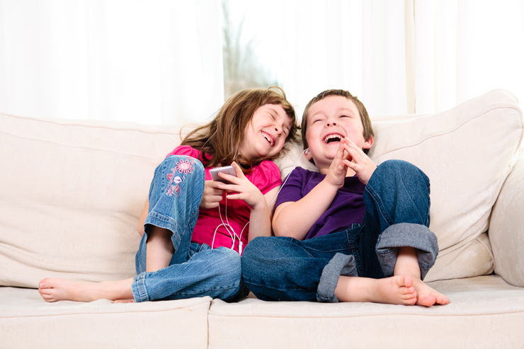 Two kids listening to music and laughing sitting on a couch