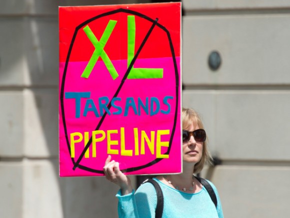 Woman holding up a protest sign that reads "xl tarsands pipeline" with an x going through it