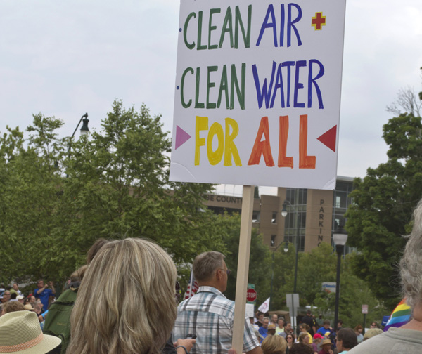 Woman marching with sign reading Clean Air Alean Water For All