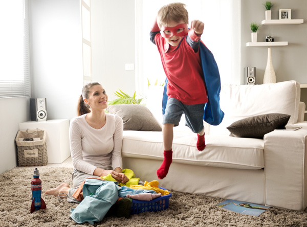 Little boy in superhero costume playing near couch
