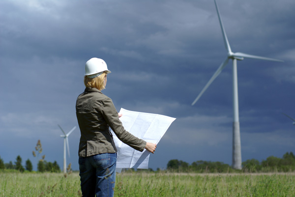 Woman in hard hat standing near wind turbine