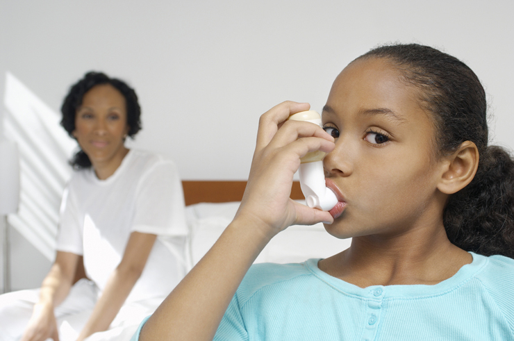 Girl using asthma inhaler with Mom in the background