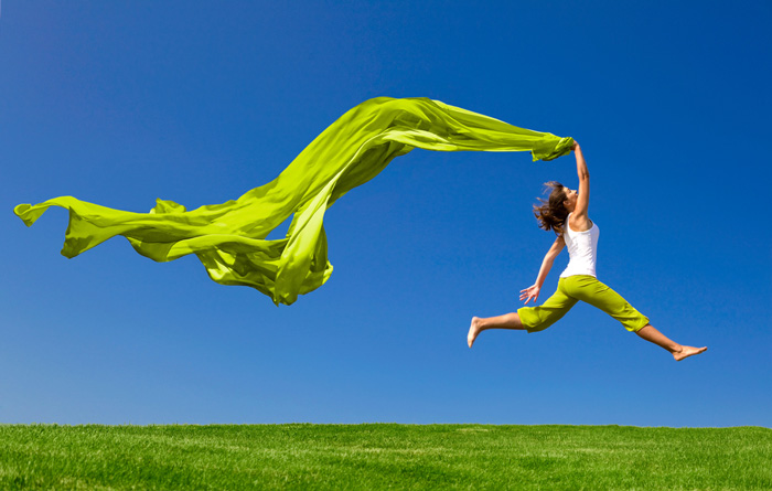 Woman running through meadow with green scarf