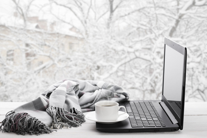 Computer, scarf and coffee inside with snowy day outside window
