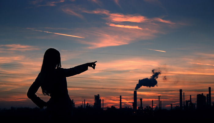 Woman pointing at a smokestack at sunset