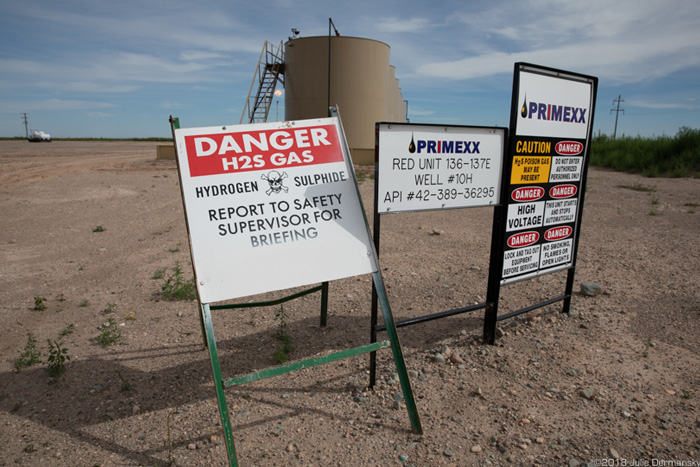 Signs warning of various hazards, including hydrogen sulfide gas, at a fracking site in the Permian Basin.