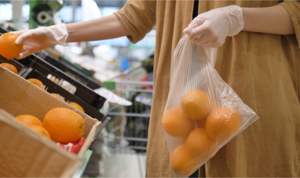 This woman putting oranges in a plastic bag and wearing plastic gloves is contributing to plastic pollution during the coronoavirus pandemic
