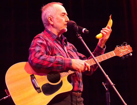 Children's singer Raffi singing on stage holding a banana