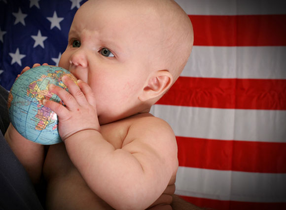 Baby in front of flag with globe in mouth
