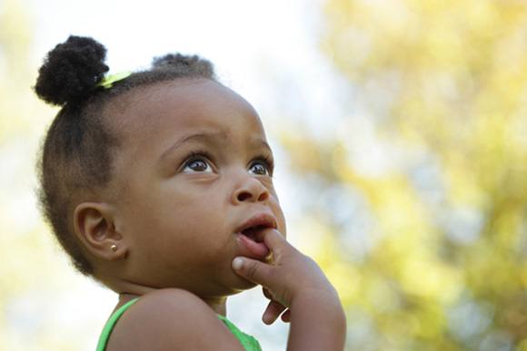 African American girl toddler with her finger in her mouth, looking toward social justice 