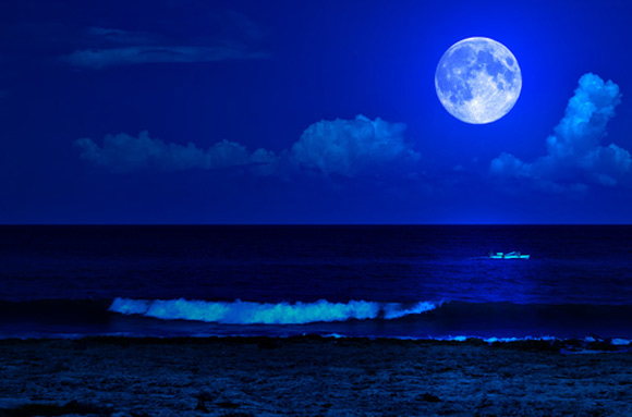 Blue photo of ocean and large full moon in the sky