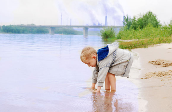 Little boy playing in water with smokestacks in the background
