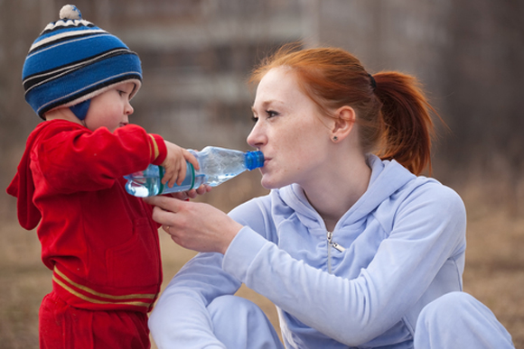 Baby holding a plastic water bottle to his mother's mouth