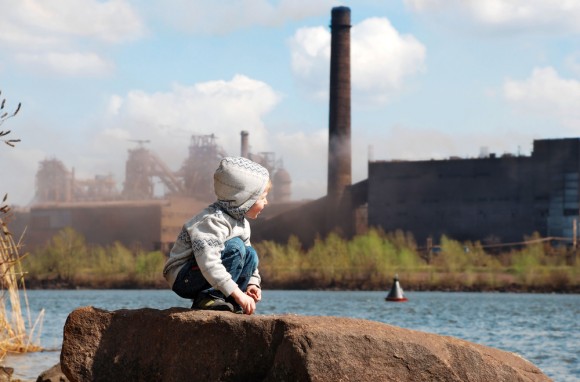 boy sitting on a rock looking across a river at a power plant