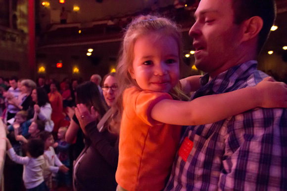 A small girl in her father's arms listens to Raffi singing