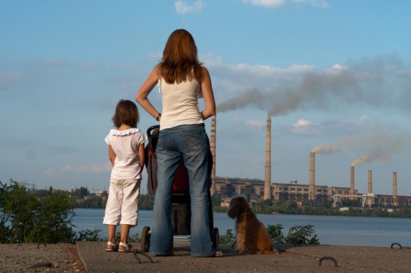family with dog standing in front of polluting smokestacks 