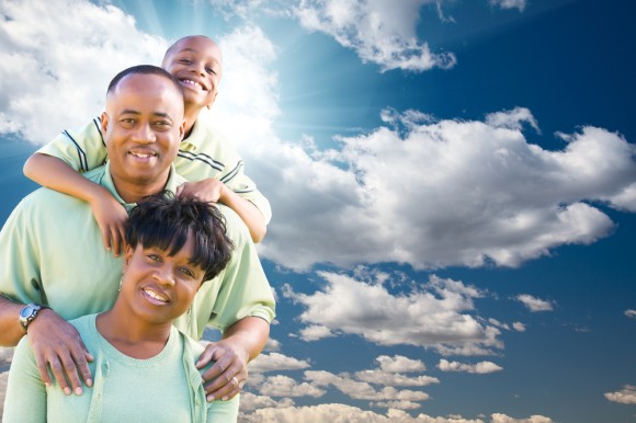Photo of an african american family standing in front of a blue cloud-filled sky 