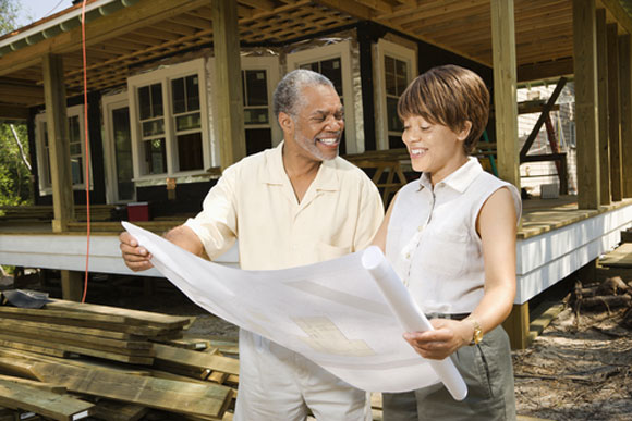 Man and woman with blueprints in front of a home under construction