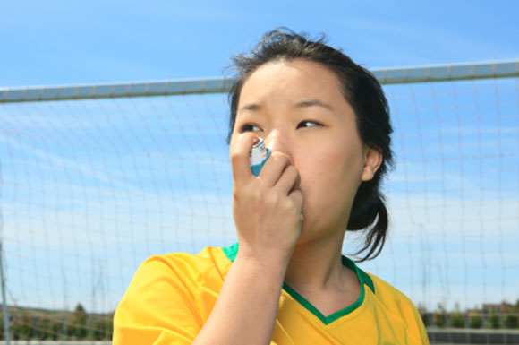 Girl standing in front of a soccer goal, using an asthma inhaler.