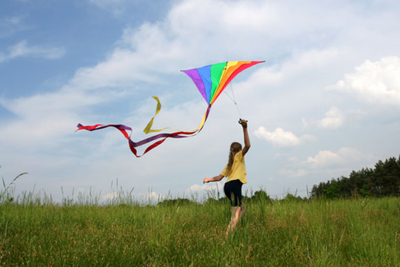 Girl flying a colorful kite in a field of grass