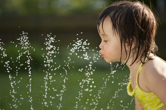 Little girl drinking from sprinkler.