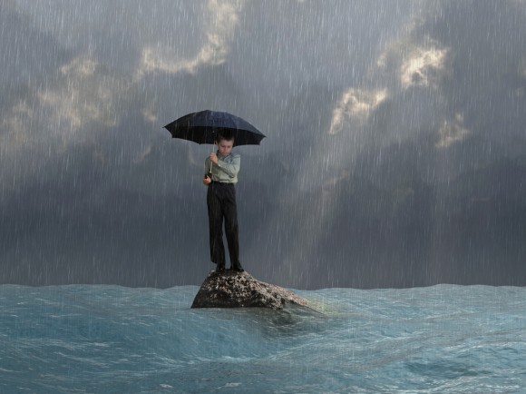 a boy standing on a rock in the ocean during a rain storm 
