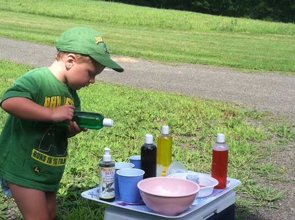 Child holding bottle of colored liquid, experimenting with other bottles of liquid